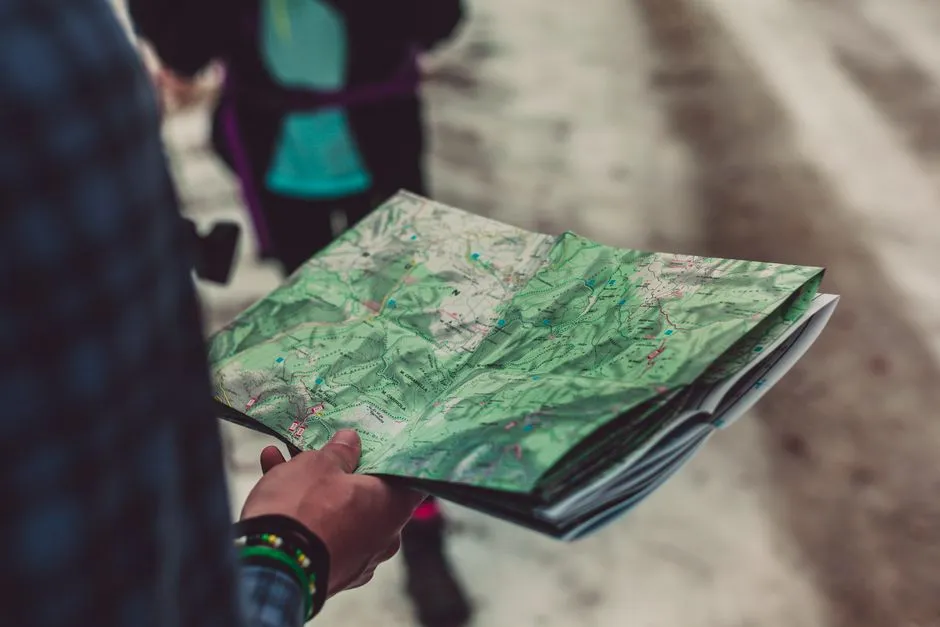 Person reading a paper trail map outdoors while route-planning a trip