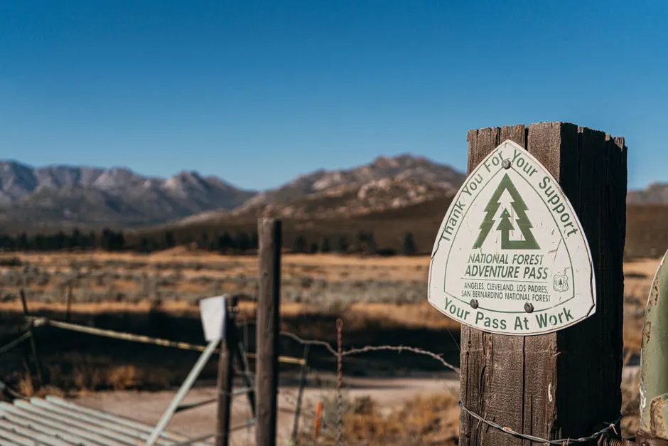 A National Forest access-pass sign on a wooden post with mountains behind it